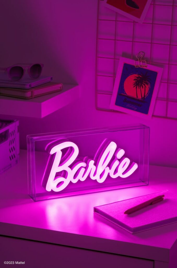 Paladone's Barbie Logo LED Neon Light is lit up pink and shown on a desk.