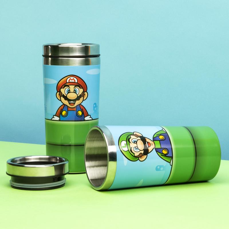 Paladone's Nintendo Super Mario Warp Pipe Travel Mug. There's two travel mugs shown to showcase the two sides of the metal cup. The Super Mario side of the travel mug is shown standing up. The Luigi side of the travel mug is shown on its side with the lid removed.